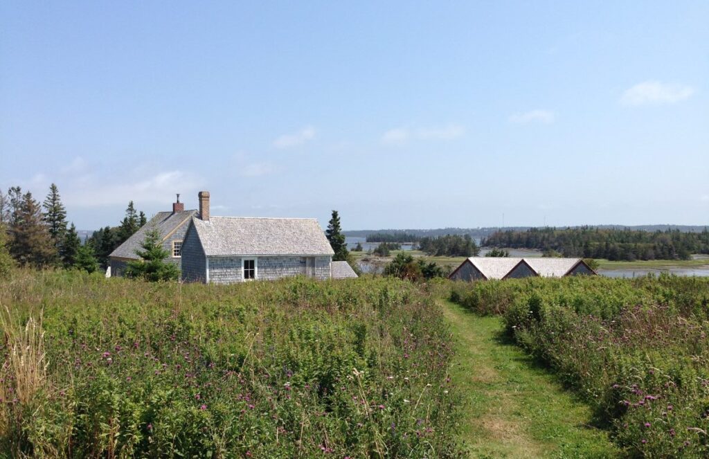 Un champ avec des maisons anciennes au loin au Village historique acadien de la Nouvelle-Écosse